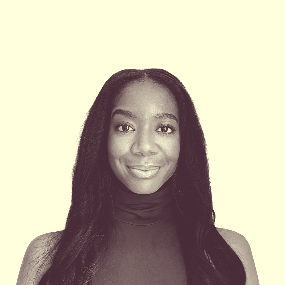 A young black woman, with a black curled hair wearing a cobalt blue sleeveless turtleneck top, smiling